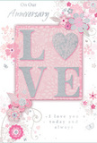 The photograph shows a softly romantic anniversary card, designed with the same care and attention to detail that a florist in Tadworth might give to an intimate anniversary arrangement. At the centre of the card's front, the word LOVE is spelled out in raised lettering, its surface coated in soft, pastel glitter that blends blush pink and silvery grey. The letters have a gentle, cushioned look and feel, offering a satisfying tactile contrast against the smooth card stock, much like the difference between velvety rose petals and cool greenery in a bouquet. The letter O is subtly echoed by a shimmering heart motif, created through the texture and sparkle of the glitter rather than a separate symbol, giving the design a sense of unity. Radiating out from this focal point, delicate blooms in blush, mauve, and pearly white open across the card in an almost watercolor softness. Their shapes are defined by fine outlines and light shading, creating the impression of petals unfurling rather than rigid, graphic forms. Slender vines, curls, and tiny leaves thread between the flowers, accompanied by miniature butterflies and swirling flourishes that add motion and a touch of whimsy, reminiscent of a breezy afternoon on the open spaces near Epsom Downs. The overall palette of pastel pinks and silvery greys creates a feeling of treasured intimacy and quiet celebration. Near the upper or central area, the phrase On Our Anniversary appears in elegant script, while the heartfelt words I love you today and always are written below in matching, understated lettering. The card's design feels composed yet tender, like a keepsake chosen to mark a shared journey of love and memories in Tadworth, perfectly pairing with a hand-delivered bouquet from Flower Delivery Tadworth.